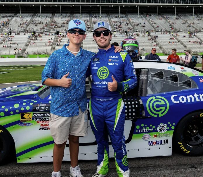 Mason Maggio and a fan pose in front of the #91 DGM Racing Chevrolet wearing the ControlAltProtect blue-and-green livery on race day